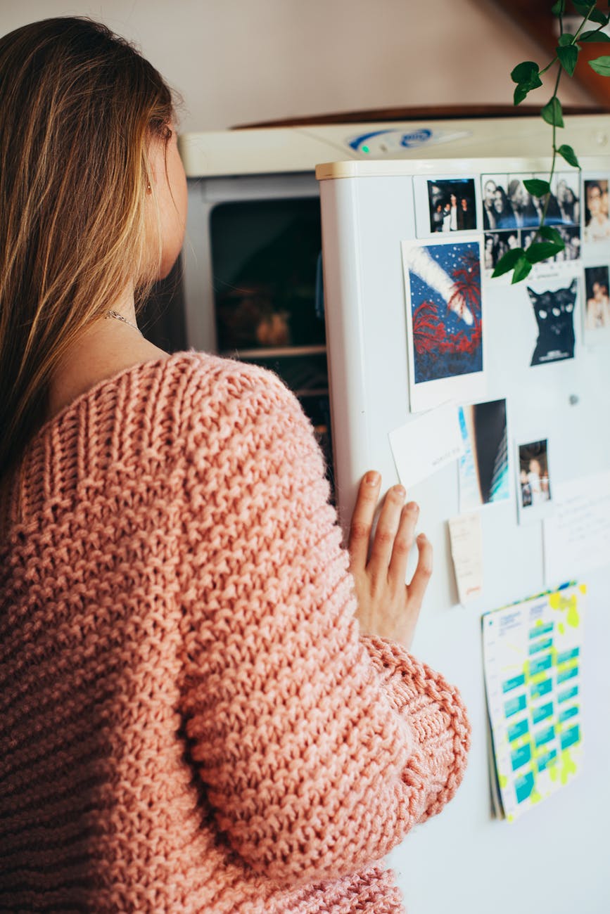 woman wearing pink knit top opening refrigerator